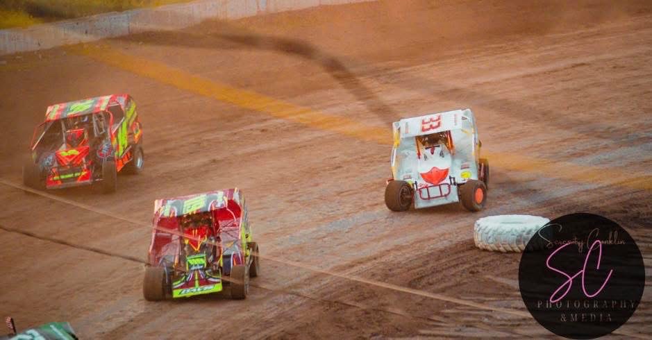 Three dirt track race cars battling side by side